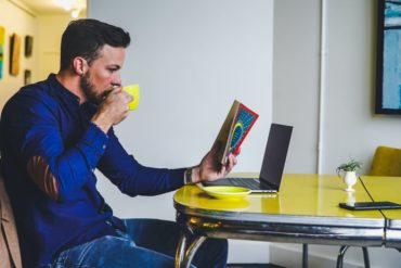 mężczyzna pijący kawę, z gazetą przed laptopem