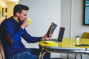 mężczyzna pijący kawę, z gazetą przed laptopem