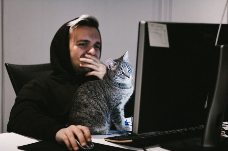 mężczyzna przed laptopem z kotem